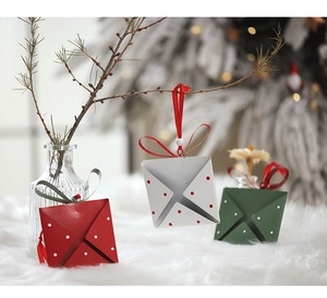 Polka dot Christmas envelope ornaments with festive ribbons on a blurred tree background