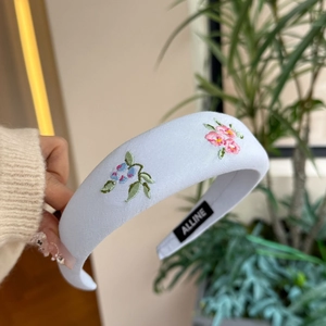 Detail of light blue padded headband with floral embroidery and Alline brand label