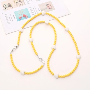 Yellow acrylic beaded crossbody strap with white hearts and silver metal clasps on a white surface
