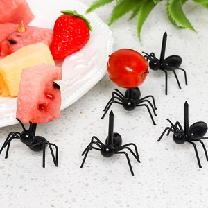 Creative black ant-shaped fruit picks carrying small fruit pieces on a white surface