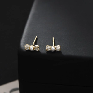Macro shot of gold bow stud earrings featuring central pearls and sparkling zircons