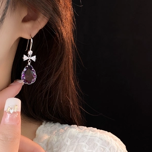 Détail de boucles d'oreilles goutte en gemme violette avec nœud argenté sur modèle