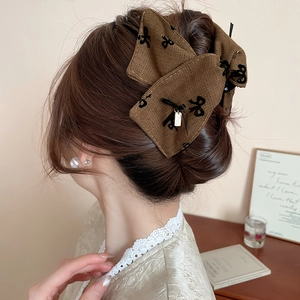 Close-up of a tweed bow hair claw with gold charm shown in an elegant hairstyle
