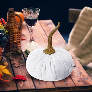 Detailed view of a white velvet pumpkin centerpiece on a rustic dark wooden dining table