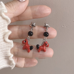 Detailed view of handmade enamel star and red pony earrings with asymmetric design