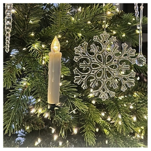 Close-up of LED candle with dripping wax and acrylic snowflake on Christmas tree