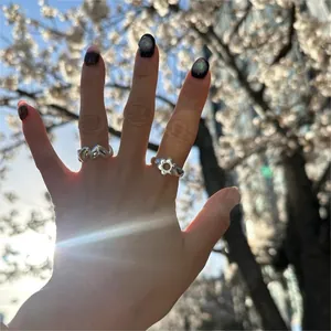 Close-up of 925 sterling silver flower and heart rings worn outdoors against cherry blossoms