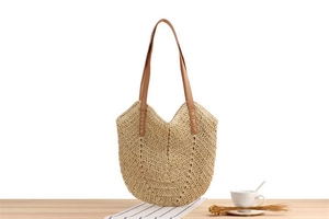 Detail of hand-woven straw shoulder bag with durable brown leather straps on a wooden table
