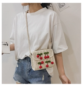 Straw square bag with red cherry details shown worn cross-body on a white shirt