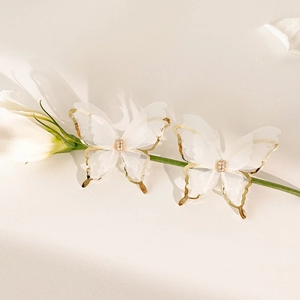 Détail de boucles d'oreilles papillon avec ailes en tulle blanc et bordure dorée