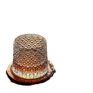Embossed glass whiskey tumbler with amber liquid and a dark wooden spinning base