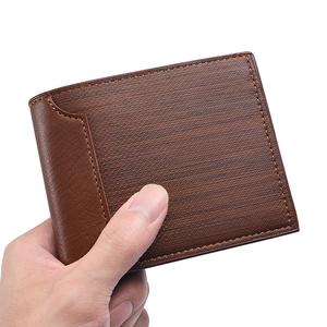 Men's bifold brown leather wallet with textured stitching being held in hand