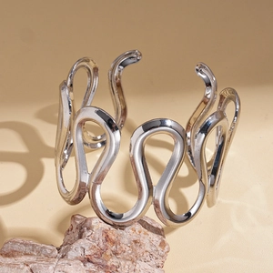 Close-up of wavy geometric open bangle with polished silver finish on natural stone