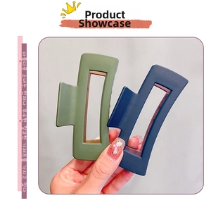 Detail of large matte green and blue rectangular hair claws held for size comparison
