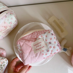 Detailed top view of pink floral quilted makeup bag with chic French label on white tray