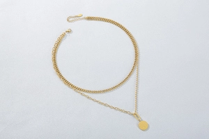 Detail of a layered golden double chain necklace with a round pendant on grey background
