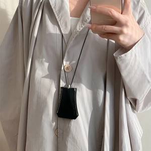 Detail of a black leather key case necklace with white stitching on a gray shirt
