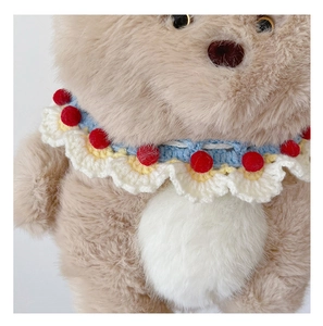 Close-up of hand-knitted ruffled collar with colorful poms on a plush teddy bear