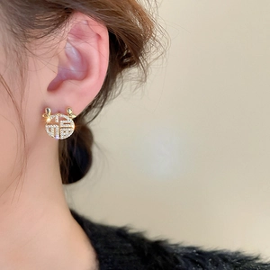 Close-up of golden Fu character earring with pavé zircon stones on earlobe