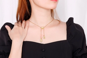 Detail of gold Y-shaped necklace with heart clasp and embossed coin pendants on a model