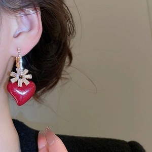 Detailed view of red heart snowflake earrings with gold plating and cubic zirconia on model