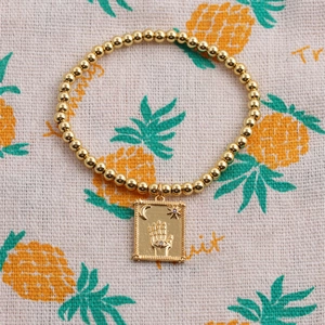 Gold plated bead bracelet with rectangle palm moon pendant on beige textile background