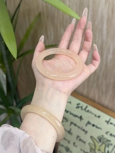 Nahaufnahme eines lichtdurchlässigen geometrischen Glasarmreifs in Beige am Handgelenk