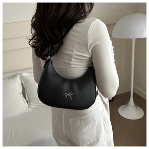 Rear view of a black crescent shoulder bag with silver bow accent on a model
