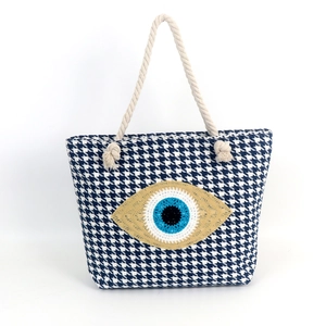 Detailed view of evil eye embroidery on blue and white houndstooth woven tote bag