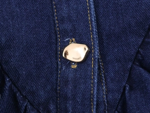 Gros plan d'un bouton pression doré irrégulier sur le tissu denim bleu foncé
