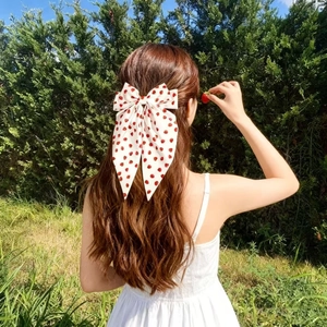Sweet strawberry print bow hair clip worn on long wavy hair in a sunny outdoor setting