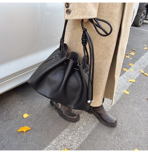 Close-up of black lychee leather bucket bag with drawstring and silver metal ball accents