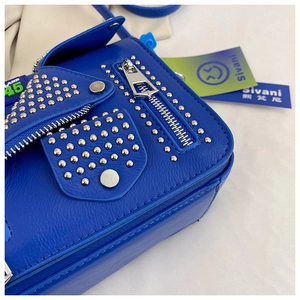 Detailed close-up of blue leather motorcycle bag with silver rivets and zipper accents