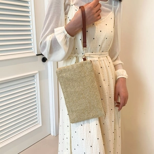 Fashionable beige straw clutch bag with wristlet strap held by a woman in a dotted dress