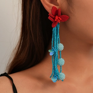 Macro detail of red fabric flower and light blue beaded tassels on drop earring