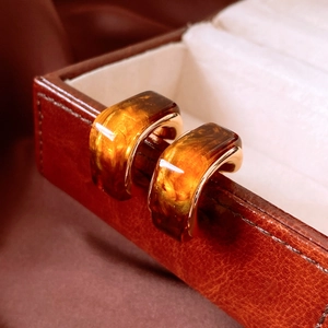 Macro shot of amber resin C-shaped earrings with golden metal edges on a leather box