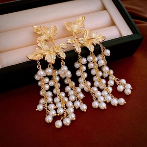 Detail of maple leaf gold earrings with hanging pearl tassels on a velvet box