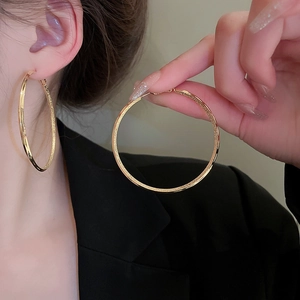 Detailed close-up of large gold-plated hoop earrings with textured finish on model