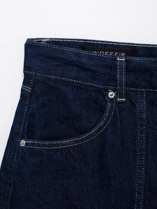 Detailed macro view of dark blue denim stitching and silver rivets on the waistband
