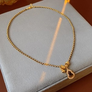 Detailed close-up of golden gourd pendant necklace with zircon and tiger eye stone inlay