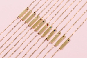 Detailed view of twelve gold bar necklaces with heart motifs and colorful birthstones
