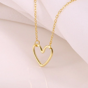 Elegant gold hollow heart necklace with delicate cross chain on white silk background