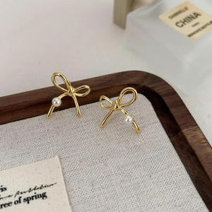 Elegant gold bow earrings with white pearls displayed on a minimalist jewelry tray