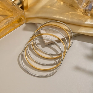 Polished gold and silver minimalist bangle set stacked on elegant marble and silk texture