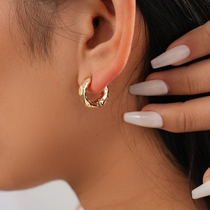 Close-up of a gold geometric hoop earring with textured metallic wave finish on ear