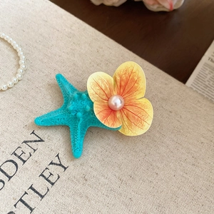 Detail of blue starfish hair clip with orange fabric flower and pearl on linen background