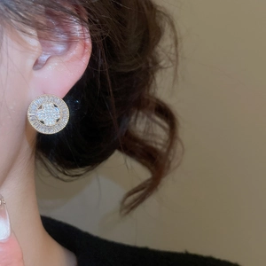 Detail of gold plated round stud earring with zircon clover and radiating baguette crystals
