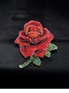 Close-up of a rose brooch with red rhinestones and green leaves on a black background