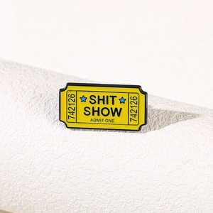 Yellow enamel ticket pin featuring black SHIT SHOW and ADMIT ONE text on white background