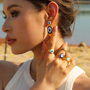 Detailed close-up of a model wearing golden evil eye earrings and rings on a beach
